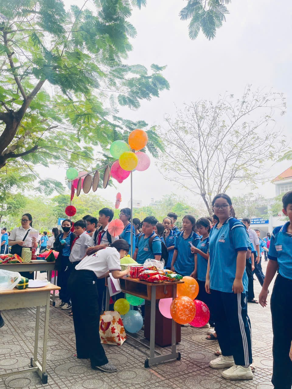 A group of people standing around a table with balloons and a table with food Description automatically generated
