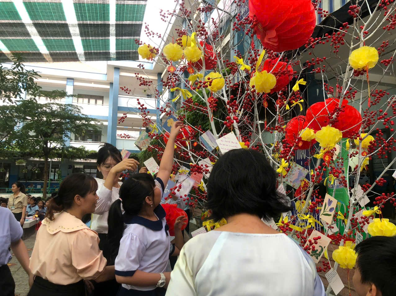 A group of people standing around a tree with paper balls and red and yellow balls Description automatically generated